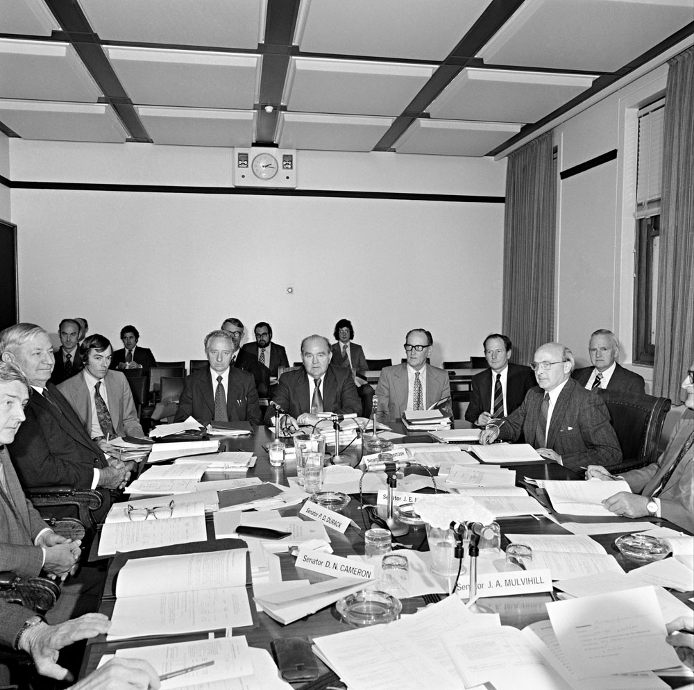 Senator the Hon Reg Bishop and officers from the Postmaster-General's Department appearing at a hearing of Estimates Committee F, 18 October 1974. Also includes Senators Peter Durack, Ellis Lawrie, Gordon McIntosh and John Marriott. National Archives of Australia: A6180, 18/10/74/92.