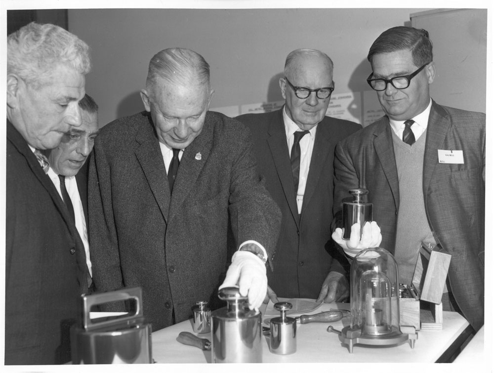Committee chair Senator Keith Laught and other committee members examining a set of calibration weights at the CSIRO National Standards Laboratory, Sydney, 1967. L-R: Senators Arnold Drury, George Poyser, Keith Laught and Archie Benn, and George Bell [Senior Principal Research Scientist, Division of Applied Physics, CSIRO].