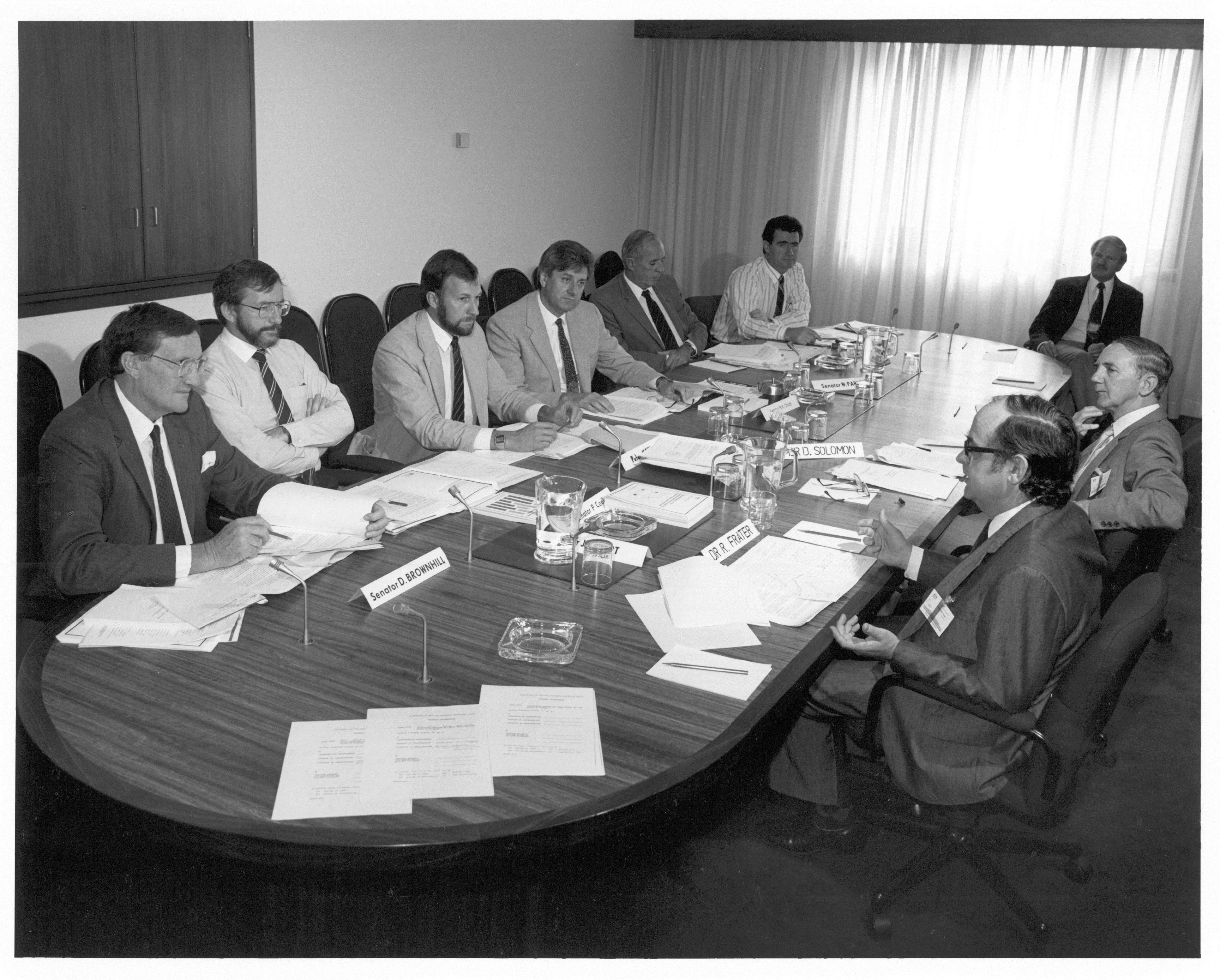 Standing Committee on Industry and Trade, 26 March 1987. Clockwise around table from left: Senators David Brownhill and Peter Cook, Peter Keele [Secretary], Senators Bruce Childs [Chair], Warwick Parer and Jim McKiernan, Michael Game [Research Officer], witnesses Dr David Solomon [Acting Director, Institute of Industrial Technology, CSIRO] and Dr Robert Frater [Chief of the Division of Radiophysics, CSIRO]. NAA: A6180, 31/3/87/66.